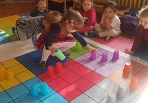 dzieci układają kubeczki na macie zgodnie z kolorem